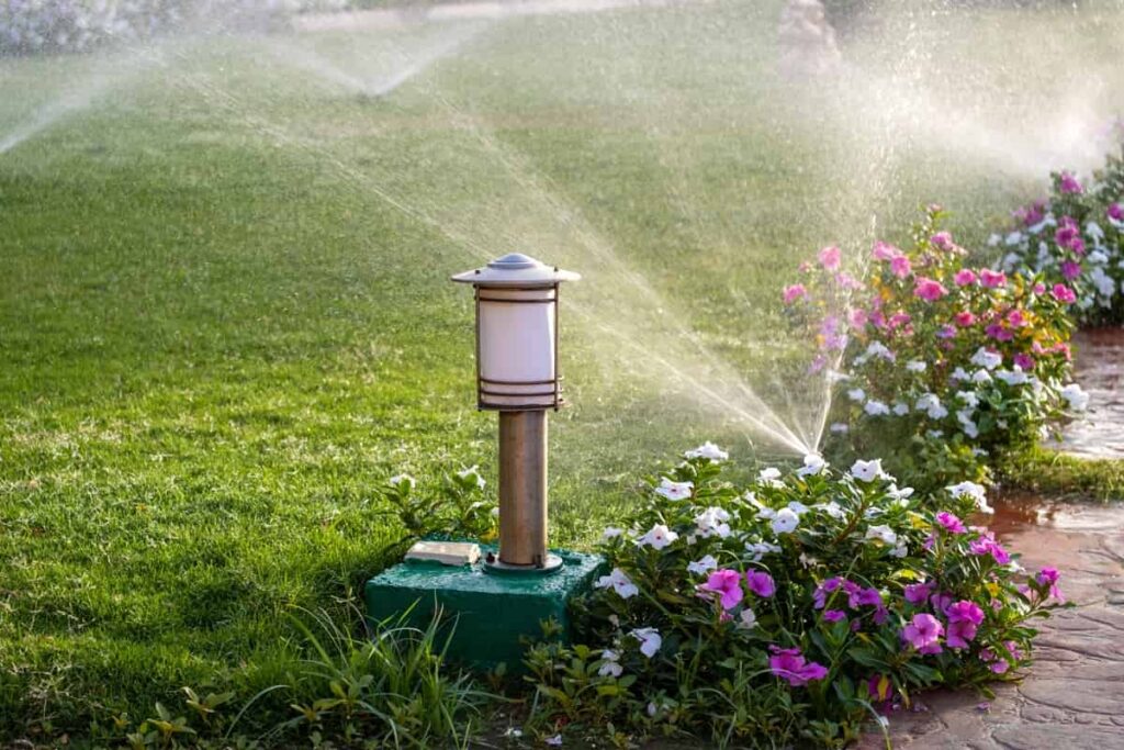 Plastic sprinkler irrigating flower bed on grass lawn