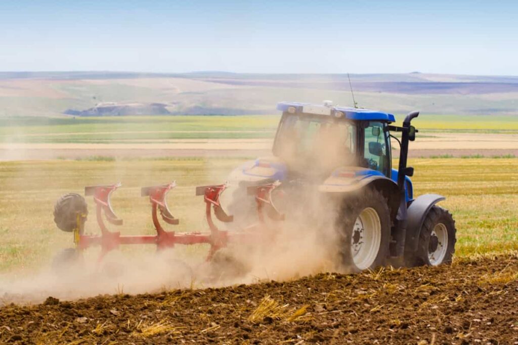 tractor ploughing a field with trail of dust